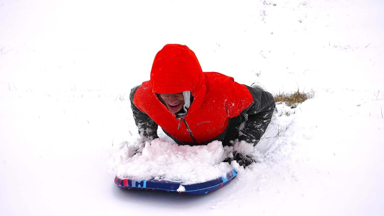 Adult enjoying winter sledding on snowy hill in vibrant red jacket.